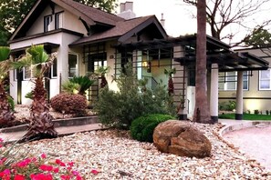 A two-story house with a garden featuring palm trees, a large rock, and red flowers. - Monte Vista Home Near Pearl | Pool & Hot Tub (San Antonio)