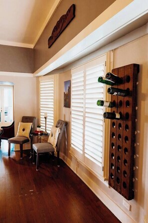 A room with wooden flooring, two armchairs, a small table, and a wine rack with bottles. - Monte Vista Home Near Pearl | Pool & Hot Tub (San Antonio)