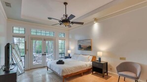 A bedroom with a bed, a chair, a nightstand, a ceiling fan, and a window.