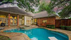 A backyard with a swimming pool, stone patio, and a wooden fence.