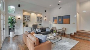 A spacious living room with a leather sofa, a glass coffee table, and a staircase leading to another level.