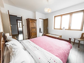 A bedroom with a bed, a wooden wardrobe, a window, and a door leading to another room.
