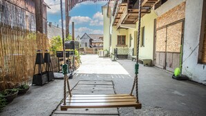 Un stretto vicolo con un'altalena in legno in primo piano, una staccionata di bambù a sinistra e un edificio con facciata in legno e una finestra a destra.