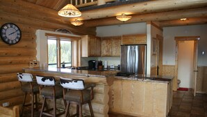 A log cabin kitchen with a central island, bar stools, wooden cabinets, a stainless steel refrigerator, and a clock on the wall. - Georgetown Lake Escape with Starlink (Anaconda)