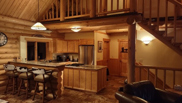 A log cabin interior with a kitchen featuring wooden cabinets, a stainless steel refrigerator, and a bar area with stools. - Georgetown Lake Escape with Starlink (Anaconda)