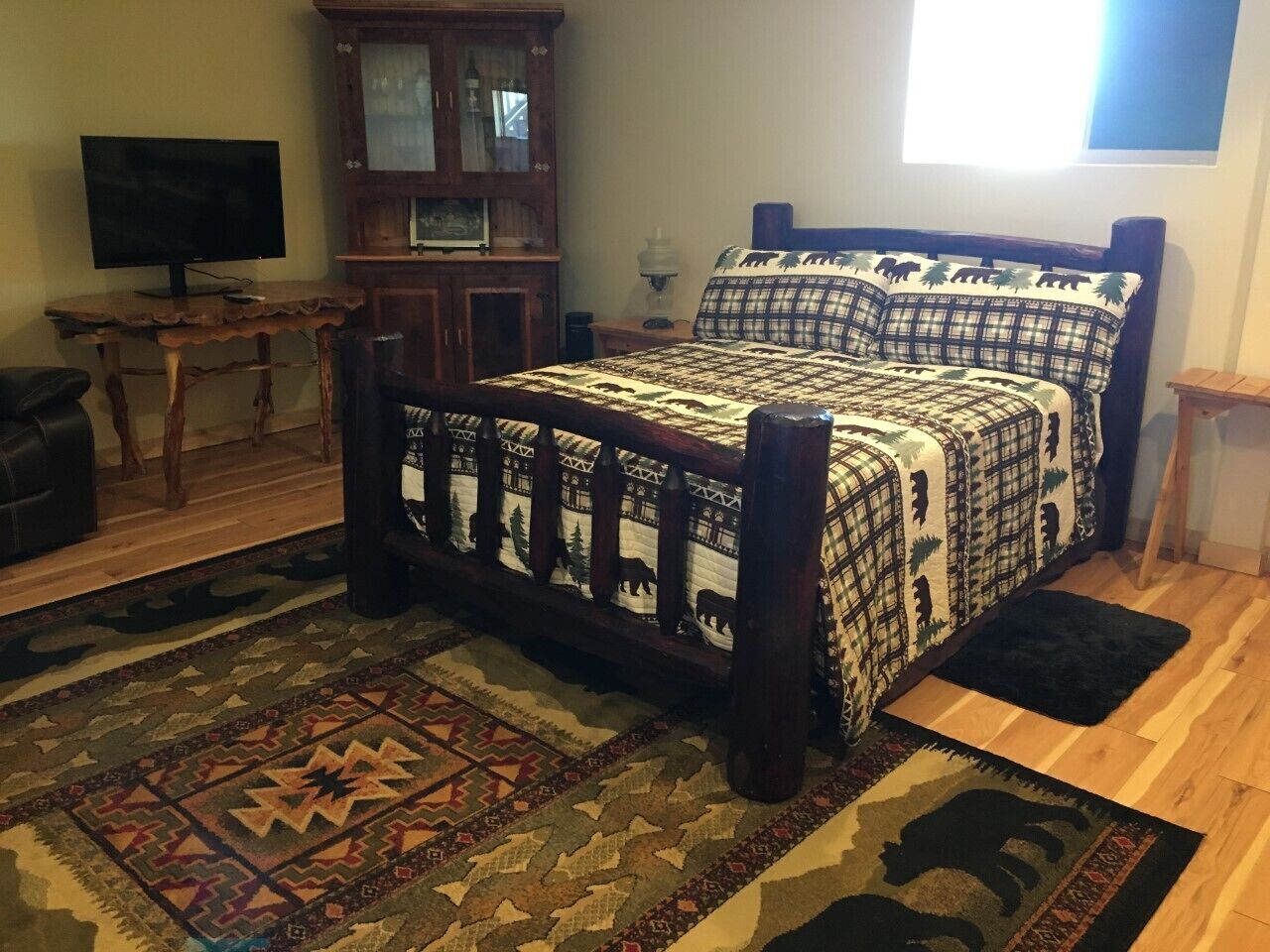 A bedroom with a wooden bed, a television on a wooden table, a cabinet, and a patterned rug.