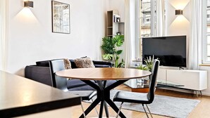 A modern living room with a round dining table, black chairs, a black sofa, a TV, and a bookshelf. - Stylish Stay in Grund with City Views (Luxembourg)