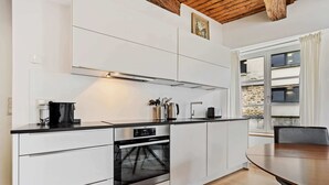 A modern kitchen with white cabinetry, a built-in oven, and a dining area with a wooden table. - Stylish Stay in Grund with City Views (Luxembourg)