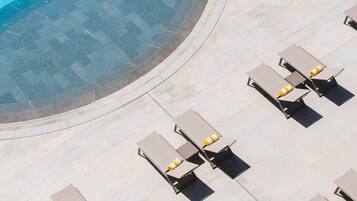 An aerial view of a pool area with a curved edge, surrounded by lounge chairs and sunbeds with yellow and white striped cushions.