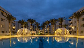 Una piscina con dos cúpulas transparentes en el centro, rodeada de palmeras y edificios.