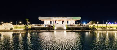 Un espace piscine avec une zone de repos au bord de la piscine et, au fond, un restaurant appelé « POOL RESTAURANT ».