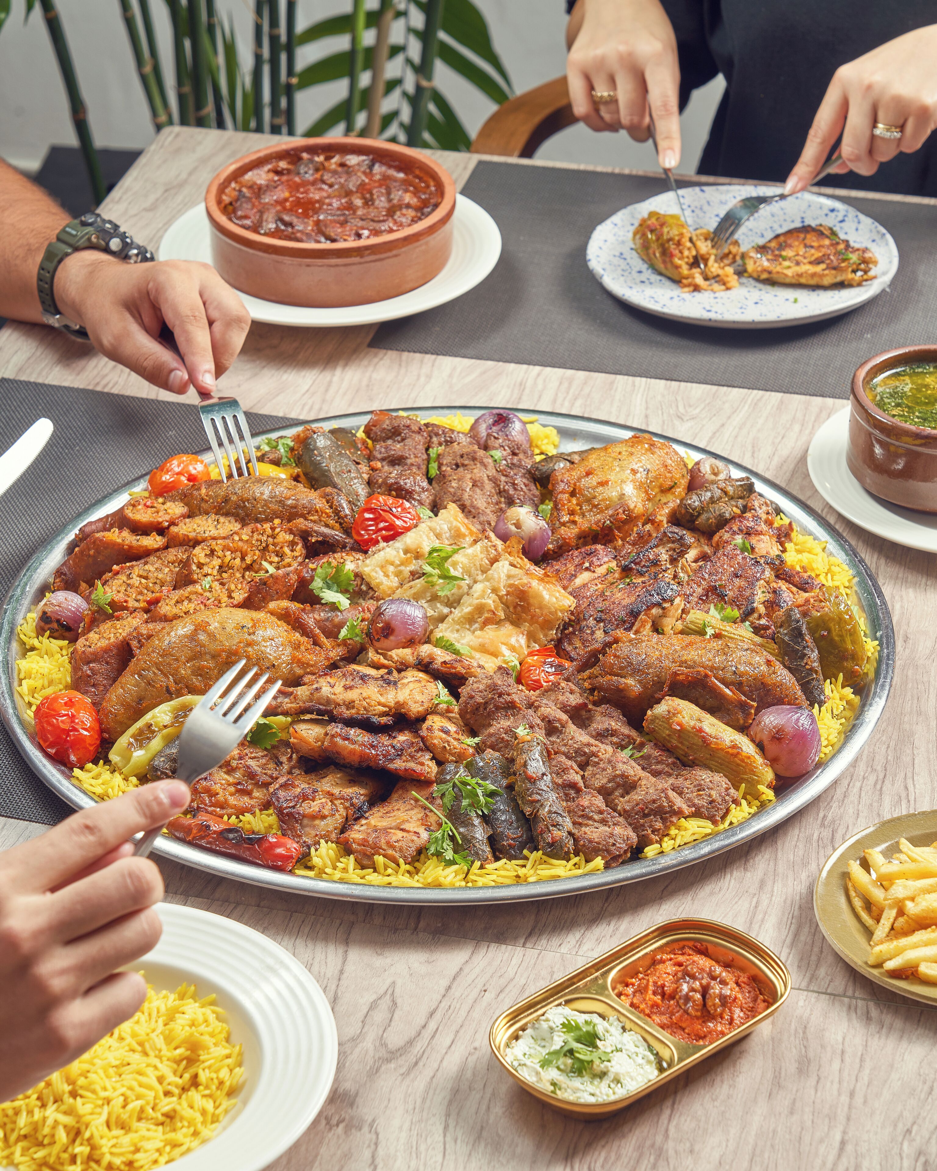 Una bandeja grande de comida con diversos tipos de carne y arroz, acompañada de guarniciones y cubiertos.