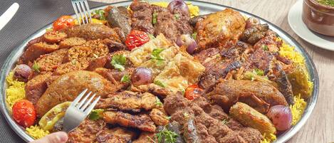 Una bandeja grande de comida con diversos tipos de carne y arroz, acompañada de guarniciones y cubiertos.
