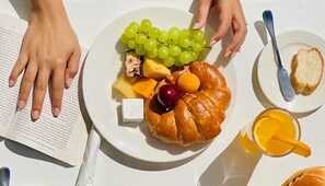 Un plato con un croissant, queso, uvas, una cereza y un vaso de jugo de naranja.