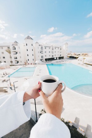 Una persona sosteniendo una taza, con vistas a una zona de piscina y un edificio al fondo.
