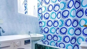Een badkamer met een wasmachine, toilet en een douchegordijn met dessin.