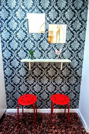 Cozy retreat with a damask-patterned wall, a shelf, a potted plant, a mirror, and two comfortable chairs.