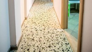 Een smalle gang met een vloerbedekking die leidt naar een kamer met een betegelde spatwand en een zithoek.