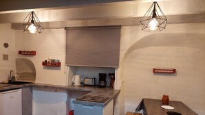 Een functionele keuken met een ingebouwde oven, een spoelbak en een koffiezetapparaat. Er staat een klein tafeltje met een tafelkleed en een bankje.