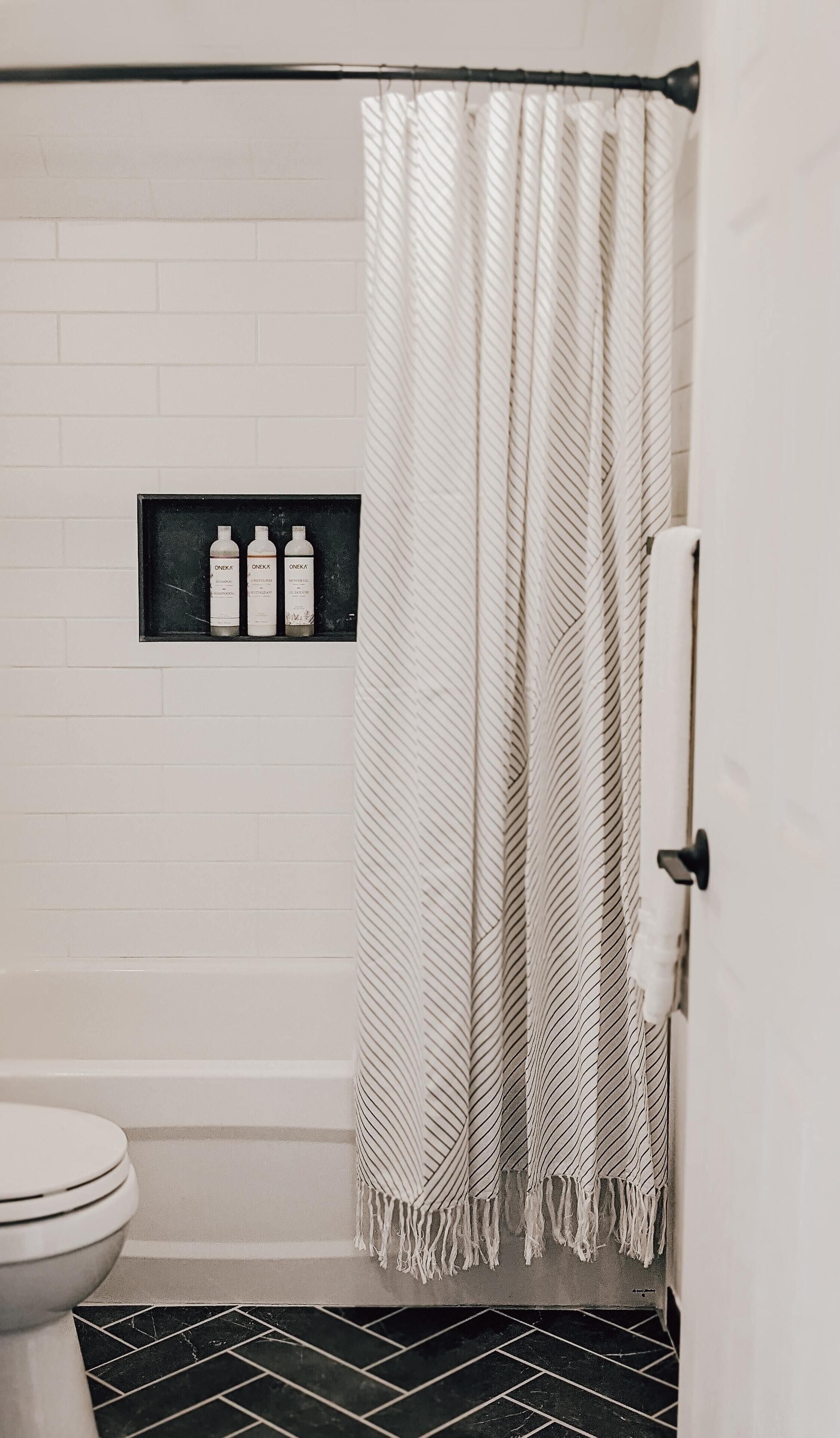 Un baño con cortina de ducha, inodoro y estante con botellas.