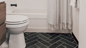 Ein Badezimmer mit einer weißen Toilette, einem schwarz-weißen Duschvorhang und einer kleinen Ablage mit drei Flaschen.
