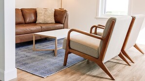 Ein modernes Wohnzimmer mit einer braunen Ledersofa, einem weißen Couchtisch und einem Holzsesselsessel mit hellem Kissen.
