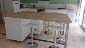 A modern kitchen with a central island, white cabinets, a microwave, a sink, and a dishwasher. - Maison Mitoyenne Avec Ascenseur (Boucau)