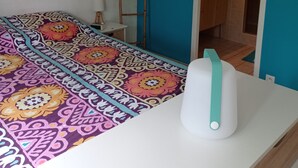 A bedroom with a colorful bedspread, a white bedside table, and a blue wall. - Maison Mitoyenne Avec Ascenseur (Boucau)