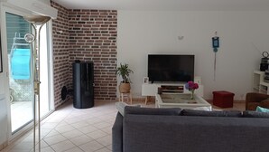 A living room with a TV, a brick wall, a sofa, and a small table with a plant. - Maison Mitoyenne Avec Ascenseur (Boucau)