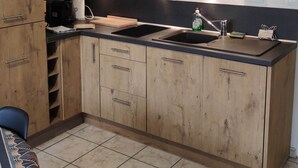 Une cuisine avec des meubles de rangement en bois, un plan de travail noir, un évier et une machine à café.