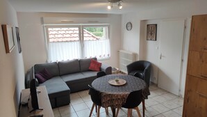 Un salon moderne avec un canapé gris, une table à manger recouverte d’une nappe à motifs et une chaise noire.