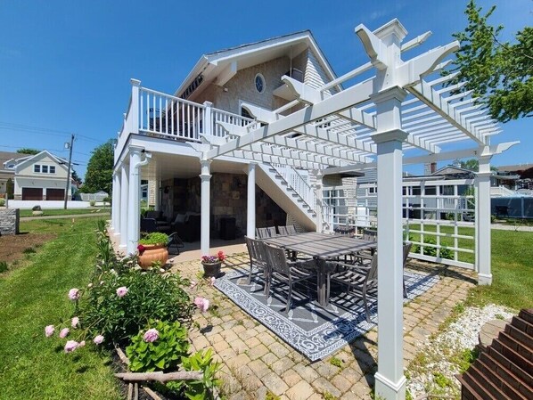 Een huis met een overdekte patio, een trap naar een balkon en een tuin vol roze bloemen.