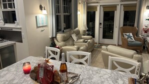 A cozy living room with a beige sofa, a wicker armchair, and a dining area with a marble table. - Beach House steps to private beaches in sought after location! (Old Saybrook)
