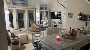 A well-lit living room with a dining area, featuring a large window, a fireplace, and a Christmas tree. - Beach House steps to private beaches in sought after location! (Old Saybrook)
