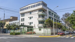 Un edificio de varios pisos con fachada blanca y detalles verdes, que cuenta con balcones y un acceso cubierto.