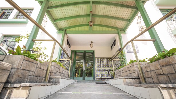 Una entrada cubierta con techo verde, paredes de piedra y suelo de baldosas que conduce a una puerta.