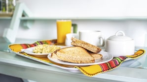 Bandeja de desayuno con tostadas y huevos sobre una mesa con un hervidor blanco y una taza amarilla.