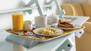 Una bandeja de desayuno con huevos revueltos, tostadas, un vaso de zumo de naranja y una tetera sobre una mesa.