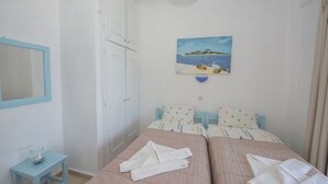 Ein Schlafzimmer mit zwei Betten, einem kleinen Tisch, einem Bild mit Strandmotiv und einem weißen Kleiderschrank.