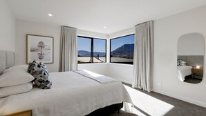 Une chambre moderne avec un grand lit, un tableau encadré, un miroir et une vue sur les montagnes par de grandes fenêtres.