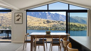 Un coin repas avec une table et des chaises, de grandes fenêtres offrant une vue sur les montagnes et un tableau encadré au mur.