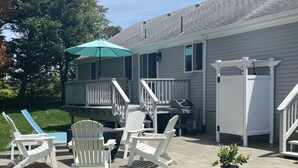 Ein Haus mit überdachter Terrasse, Adirondack-Stühlen, einem Tisch, einer kleinen Terrasse mit Geländer und einem Blumentopf.