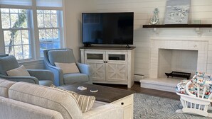 Ein Wohnzimmer mit einer Couch, Sesseln, einem Couchtisch, einem Fernseher, einem Kamin und einem gemusterten Teppich.