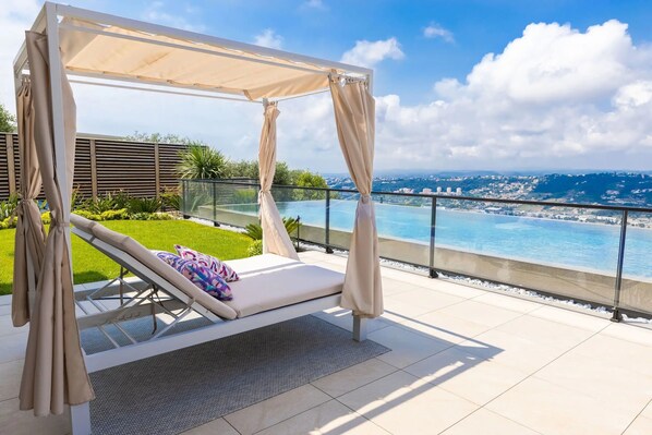 Un balcon doté d’un auvent, d’un fauteuil de relaxation et offrant une vue sur une piscine et le paysage urbain.