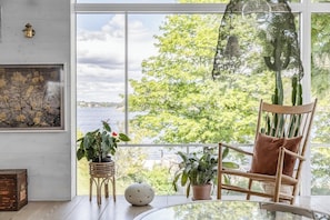 Une pièce dotée d’une grande fenêtre, d’une chaise en bois, d’une table et de diverses plantes en pot.