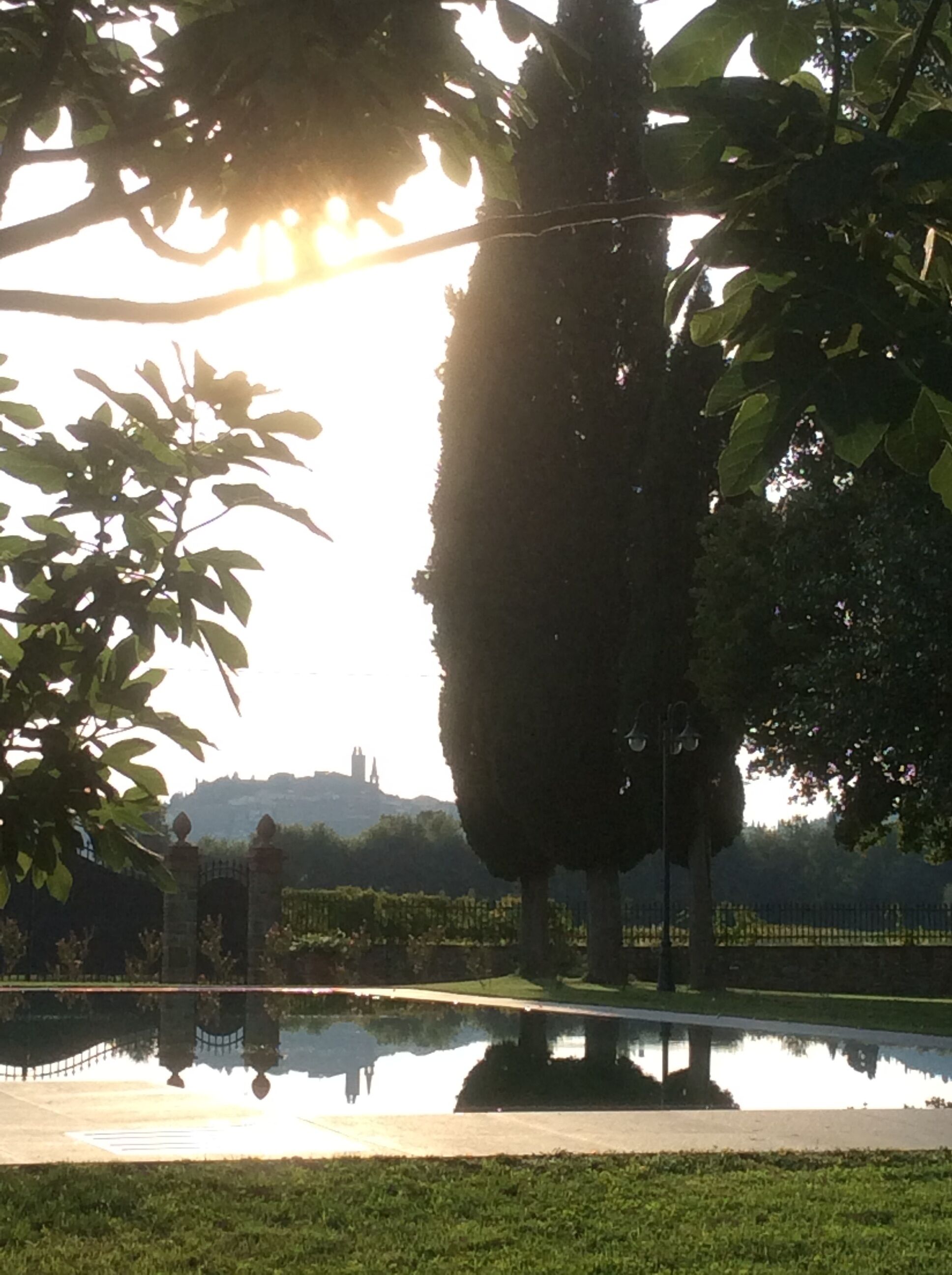 Un parc avec un étang dans lequel se reflètent les arbres et un bâtiment situé au loin.