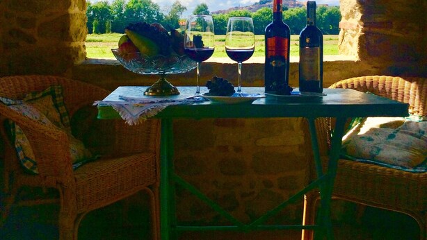 Ein Tisch mit Weinflaschen und Gläsern, platziert in einem Raum mit einer Ziegelbogenarchitektur und Blick auf eine schöne Landschaft.