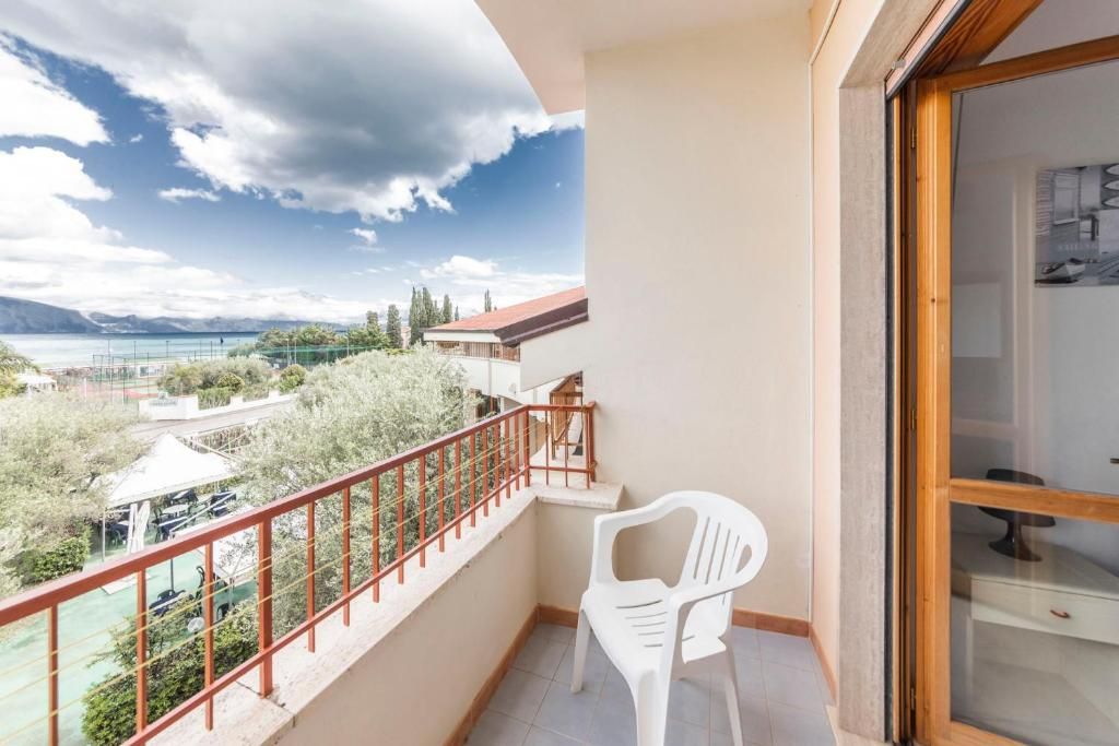 Un balcone con vista su un lago e montagne, una sedia di plastica bianca e una porta in legno.
