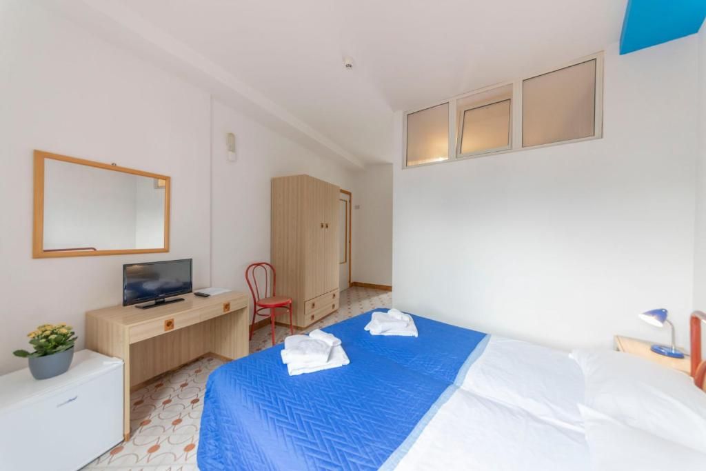 A hotel room with a bed, a desk with a television, a wardrobe, and a mirror on the wall.