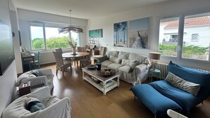 Un salon spacieux avec une grande fenêtre, un coin repas et un canapé bleu.